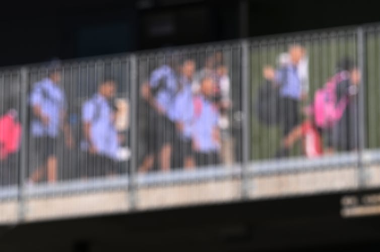 A blurred photo of young students walking across a bridge.