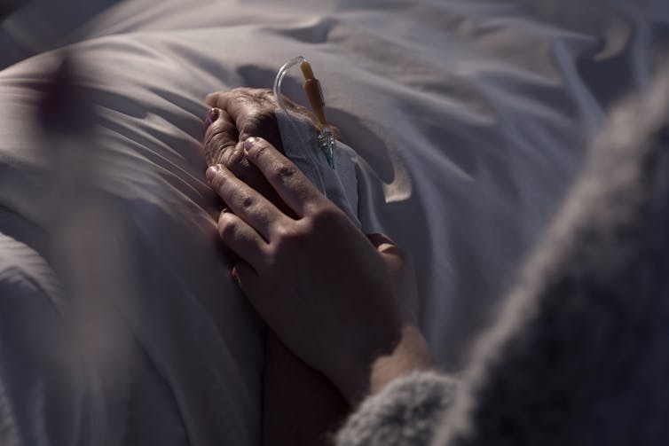 One hand holds another on a hospital bed.