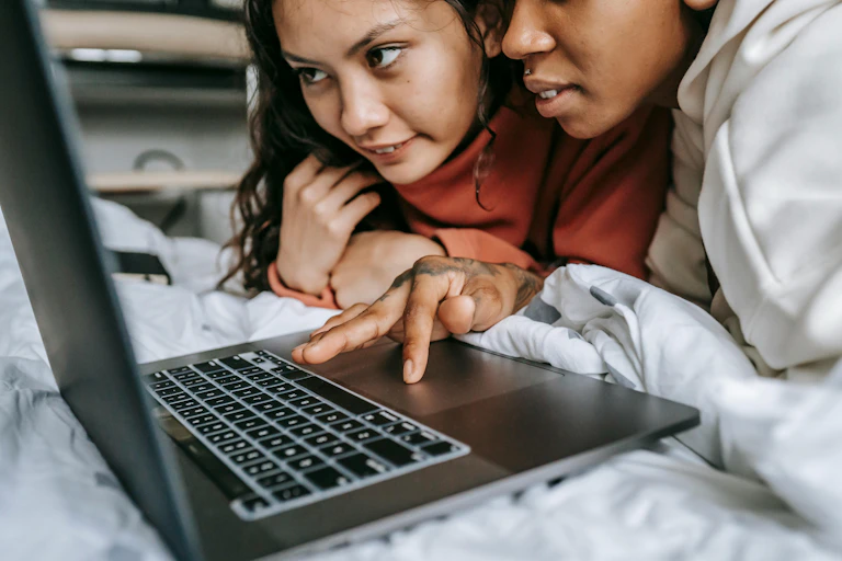 Two young women looking at laptop on bed