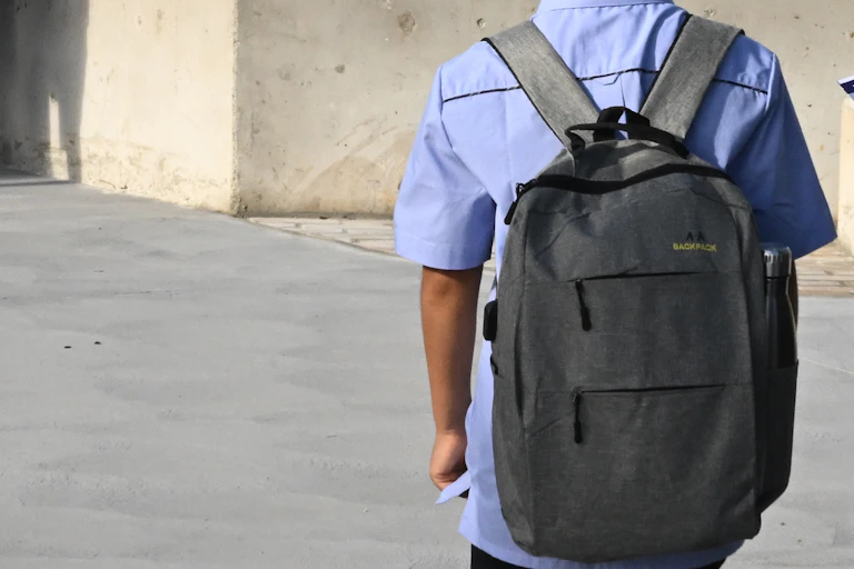 A young student in uniform with a backpack, standing on their own.