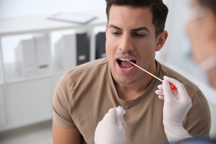 Health worker in clinic wearing gloves holding a swab near man's mouth