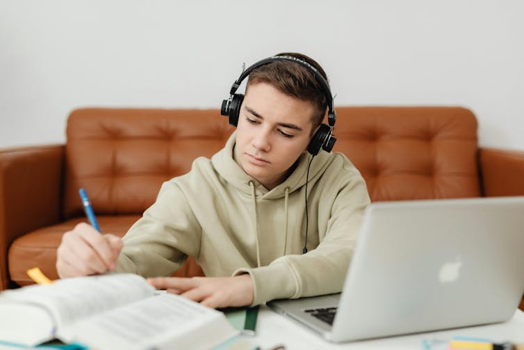 A teenage boy wears headphones while he studies next to a couch.