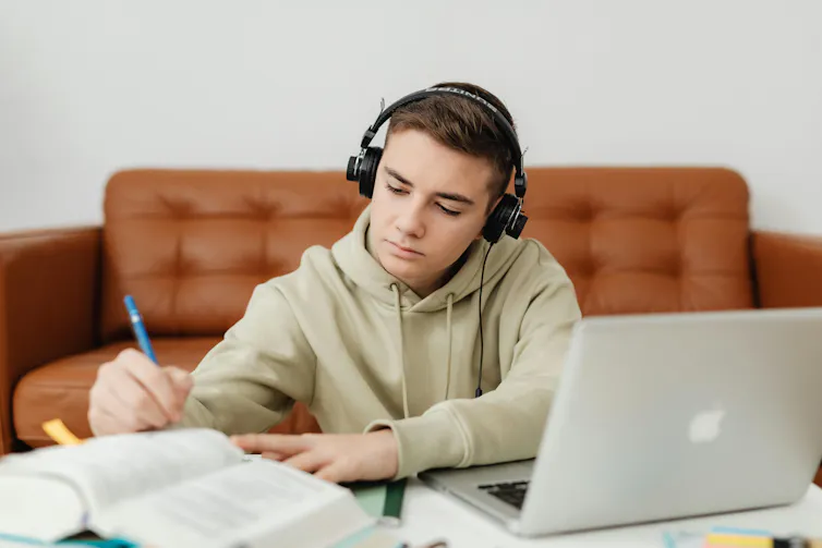A teenage boy wears headphones while he studies next to a couch.