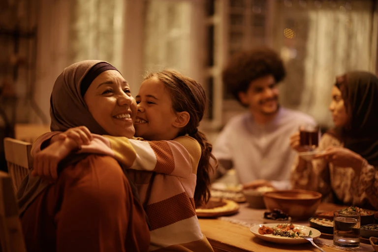Muslim woman wearing headscarf hugging child at dinner table