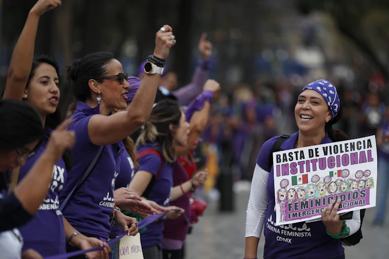 Women wearing purple shirts at a protest. One carries a sign in spanish