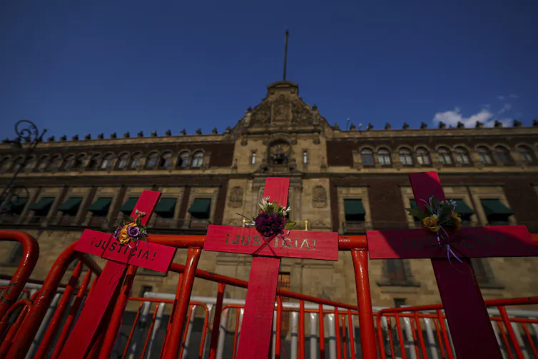 Red crosses with the word justice written in Spanish in front of a large stone buidling