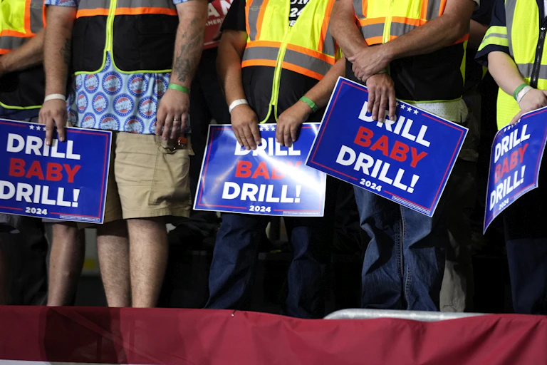 People stand in a row carrying placards that read: drill baby drill