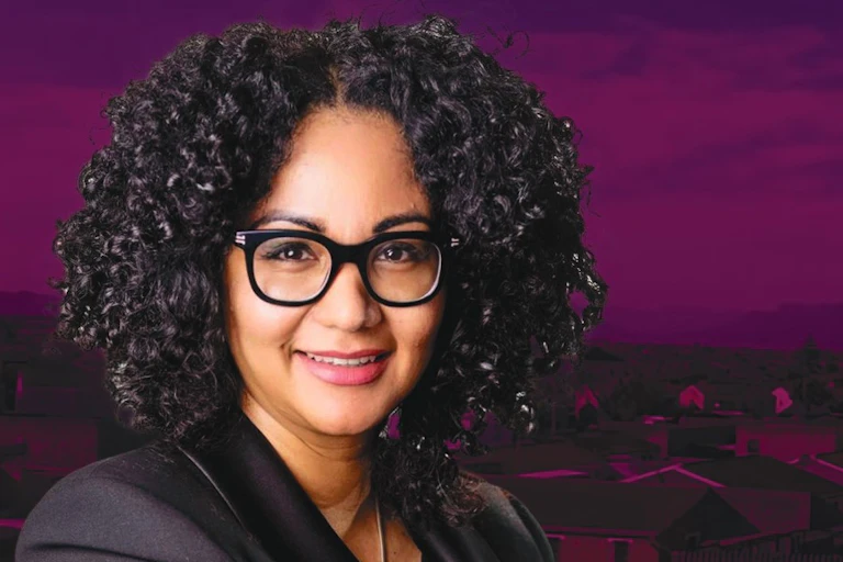A portrait of a smiling woman against a purple background in which houses and other buildings are visible