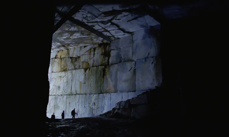 Three humans looking tiny inside the huge Carrara marble quarry in Italy.