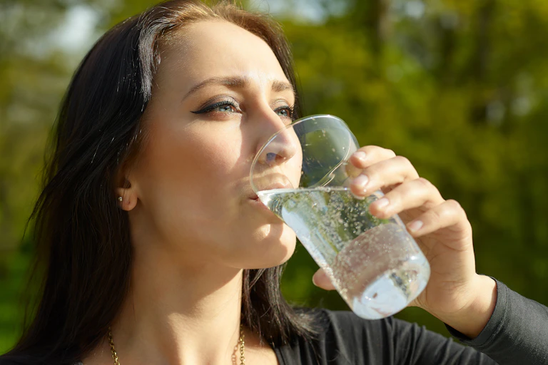 A woman drinks a glass of sparkling water.