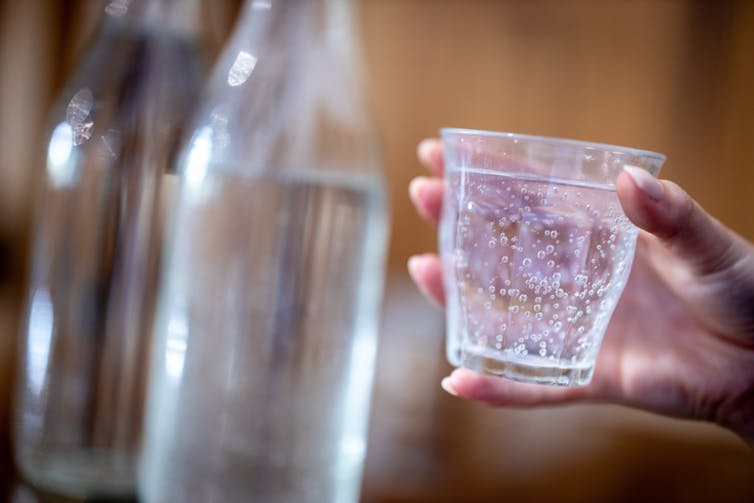 A hand holds a glass of sparkling water.