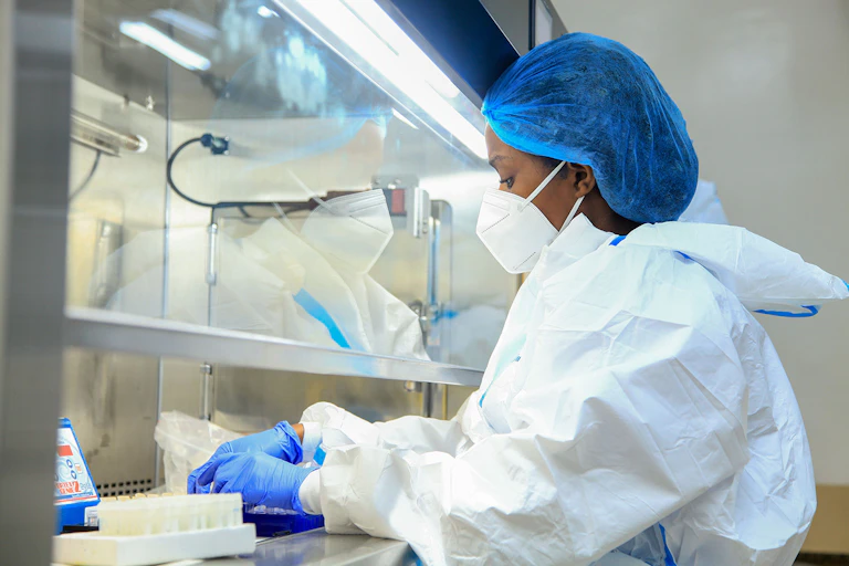 Woman in laboratory, dressed in protective cap, face mask, overall and gloves