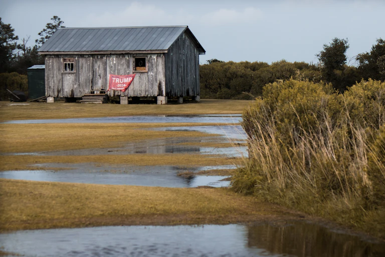 A building with a Trump flag behind pools of floodwater.