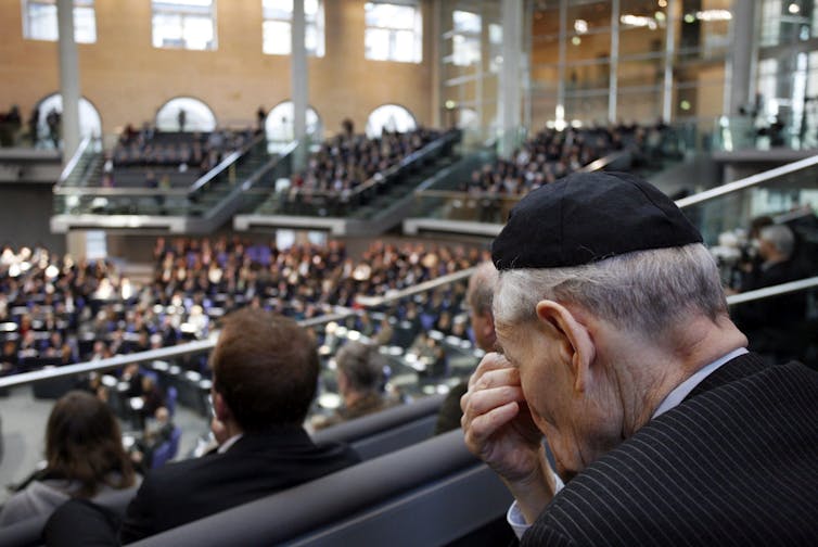 A man in a kippah / skullcap seen with eyes covered sitting in an assembly.