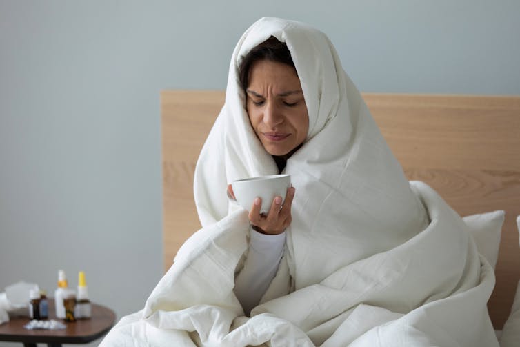 A woman with a head cold is wrapped in a duvet.