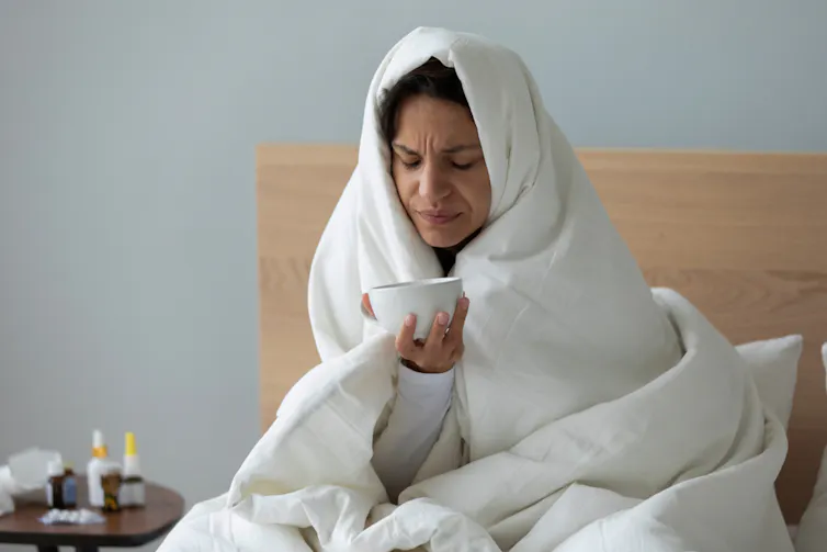 A woman with a head cold is wrapped in a duvet.