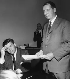 Black and white photo of a man in a suit holding a sheaf of papers