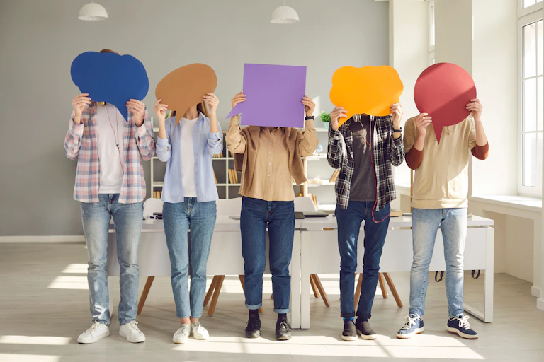 People stand in a row carrying cut outs in the shape of speech bubbles in front of their faces