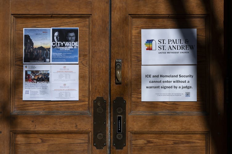 Two signs on a set of church doors, one of which says 'ICE and Homeland Security cannot enter without a warrant signed by a judge.'
