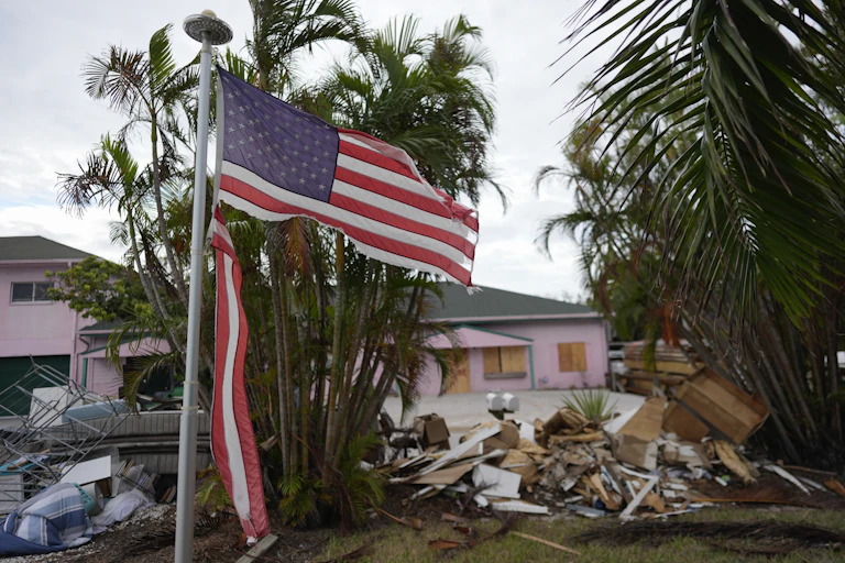 a tattered American flag flaps outside a home with furniture and household items damaged