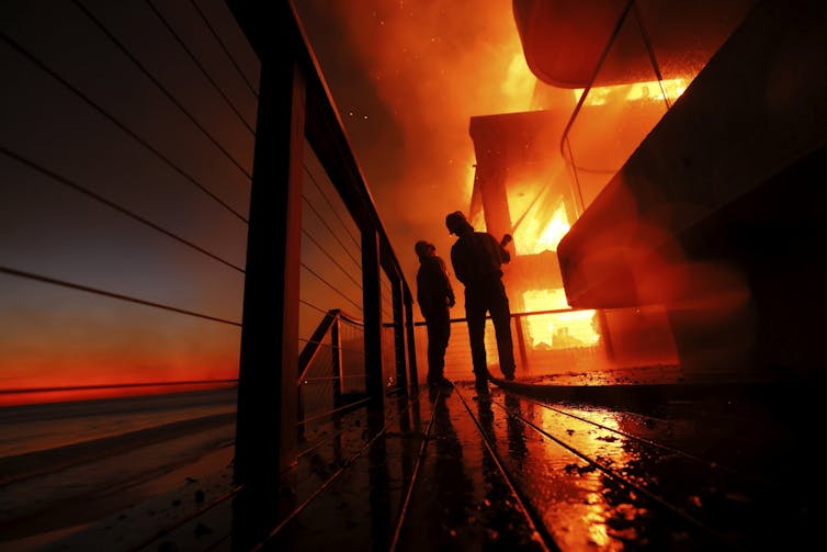 two firefightes silhouetted against a burning building