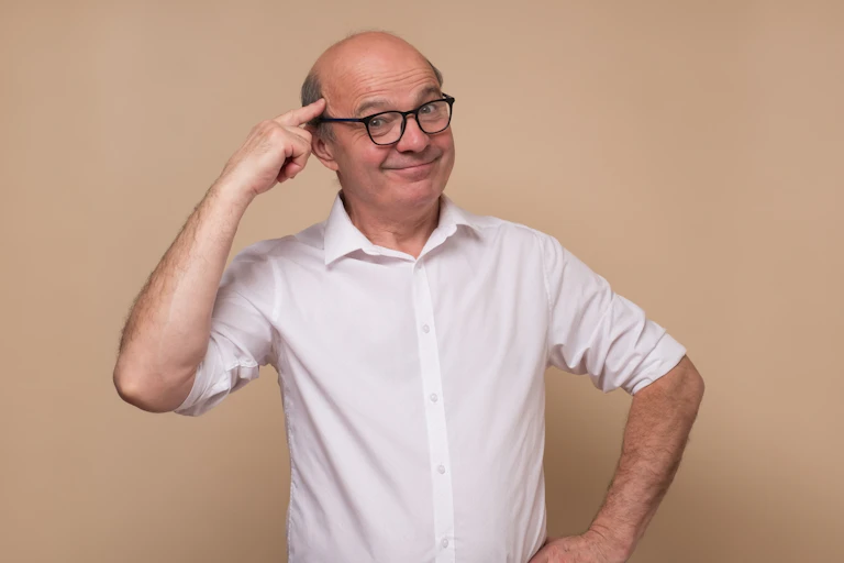Middle aged man in glasses pointing to his brain.