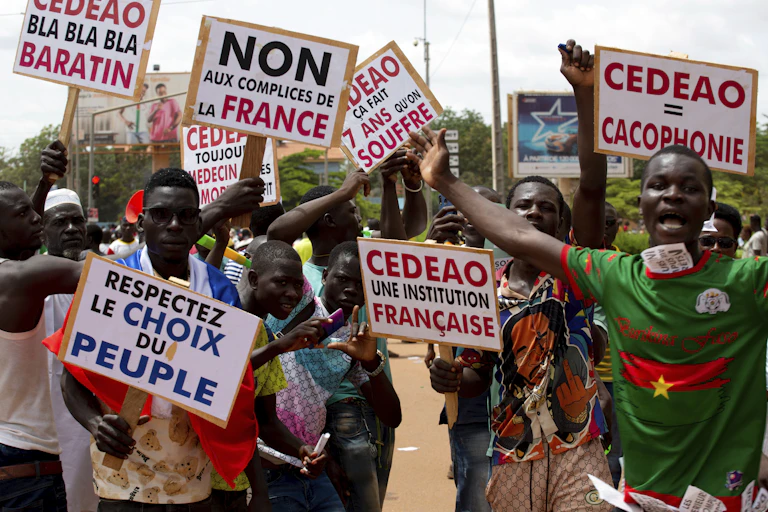 People at a protest carry signs in French that read: No to compliance with France and respect the choice of the people