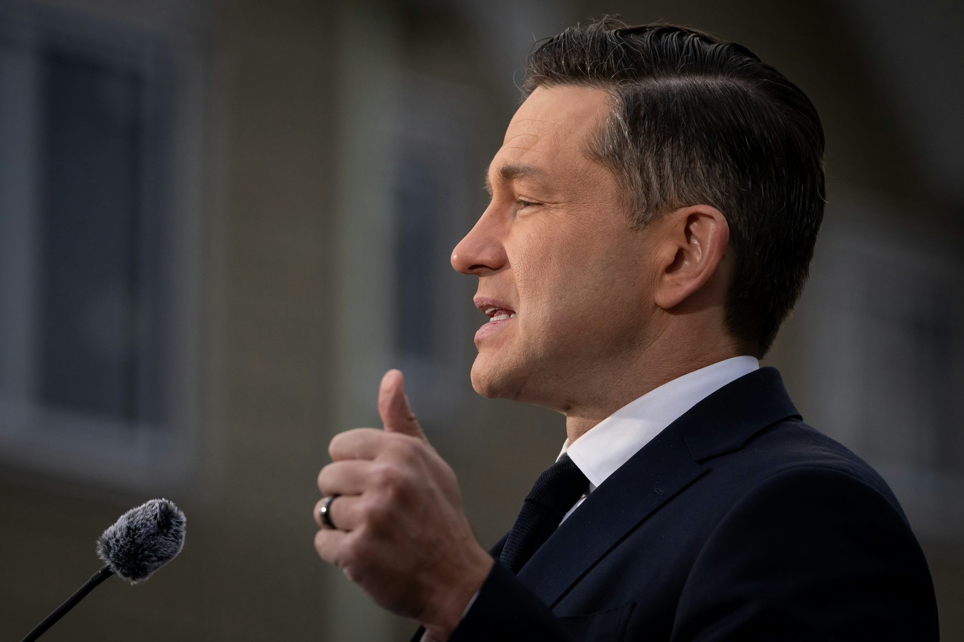 A dark haired man in silhouette speaks into a microphone.