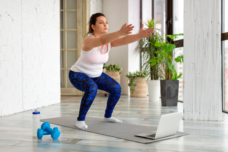 A woman performs a body weight squat on a yoga mat indoors.