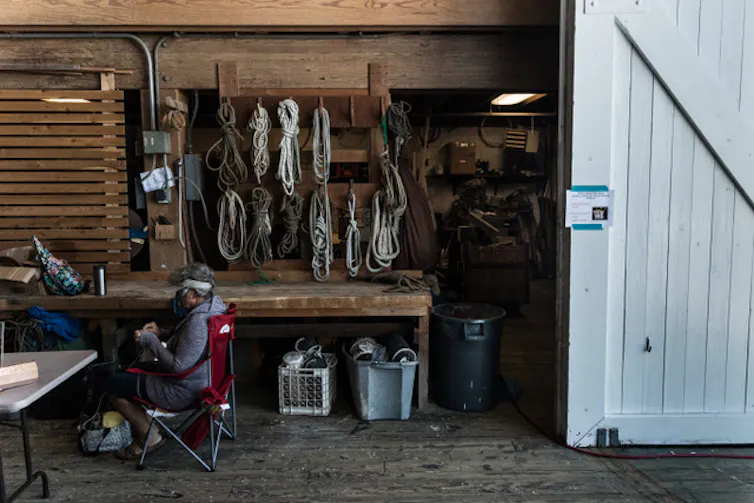 A person sits mending rope in a workshop.