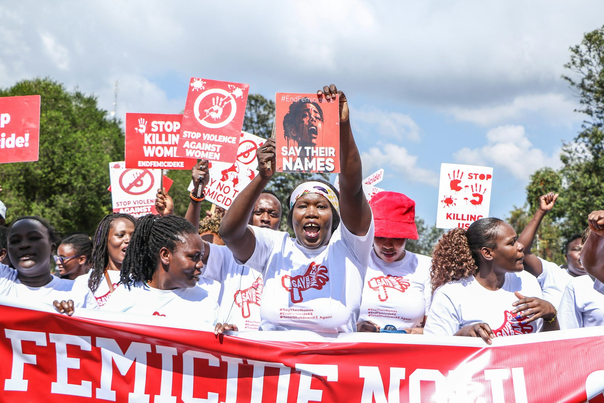 Women dressed in white T-shirts walking in a group and holding up posters written 'stop killing women' 'say their names'