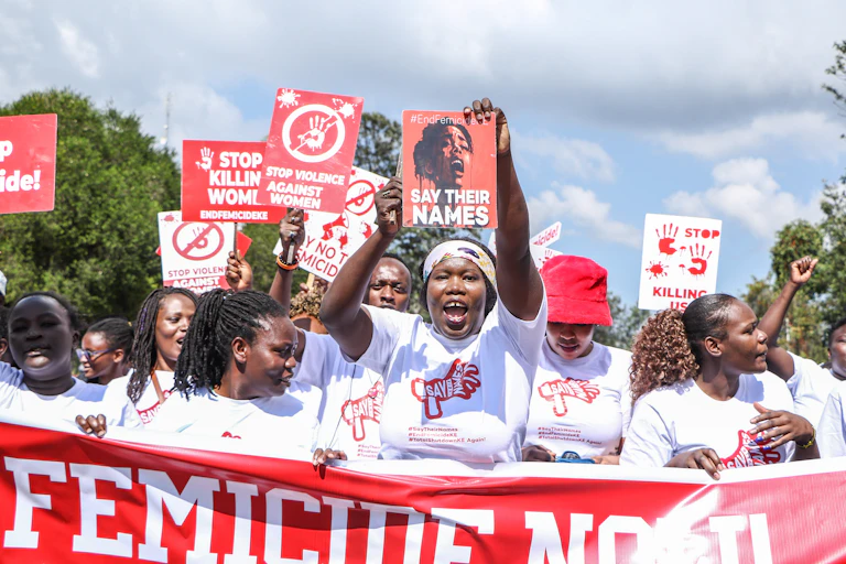 Women dressed in white T-shirts walking in a group and holding up posters written 'stop killing women' 'say their names'
