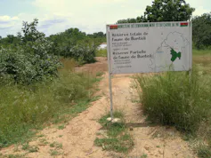 A dusty track with bushes, trees and shrubs dotted through the grass and the sign of the Bontioli nature reserve
