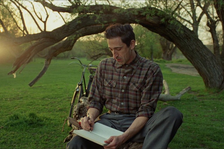 A man sat under a tree draws in a notebook.