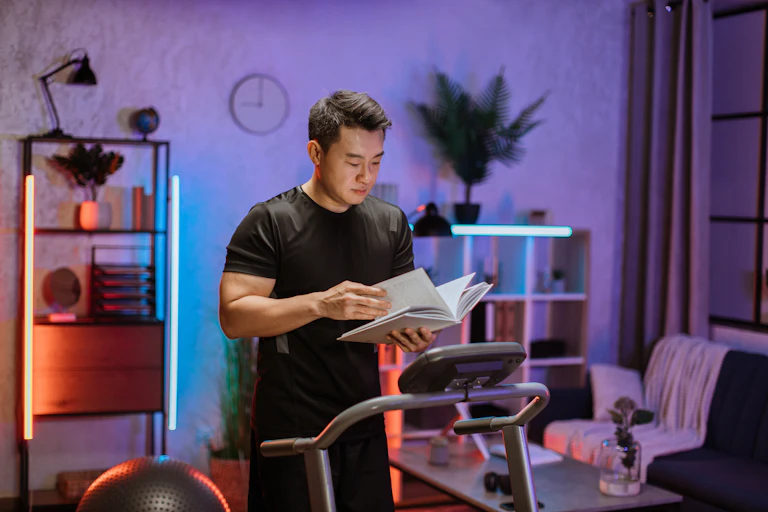 Homem lendo um livro enquanto faz exercícios físicos, correndo em uma esteira