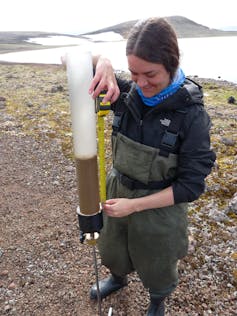 une femme se tient sur un sol rocheux avec un tube à moitié rempli de sédiments