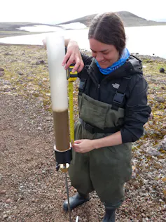 a woman stands on rocky ground with a tube half-filled with sediment