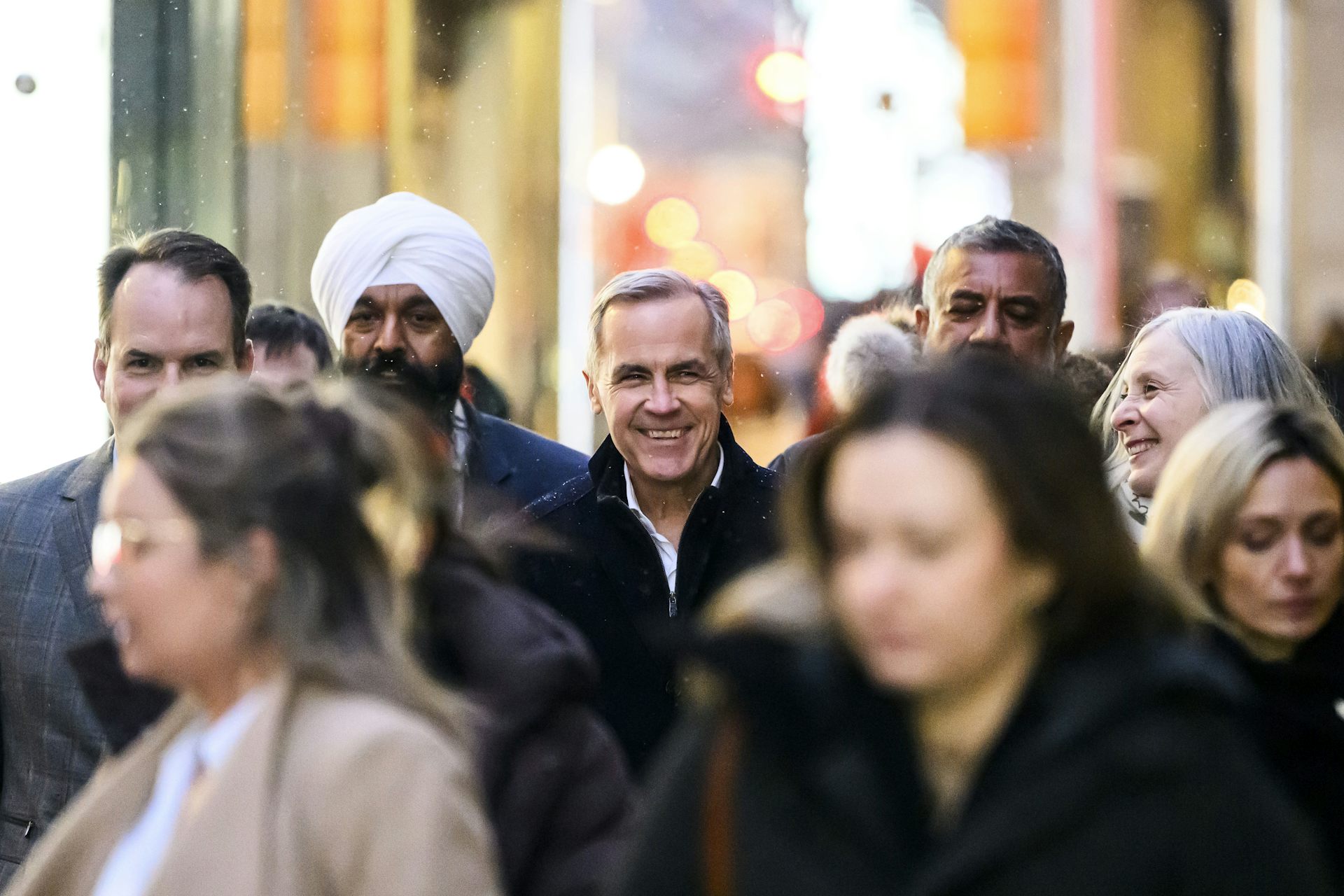 A smiling man in the midst of several people in blurred focus.