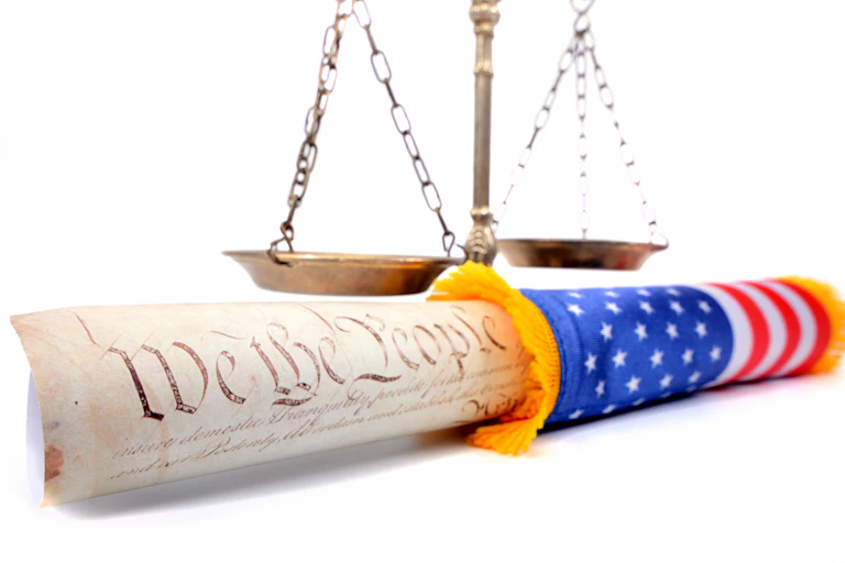 A copy of the Constitution is rolled into a US flag and in front of scales.