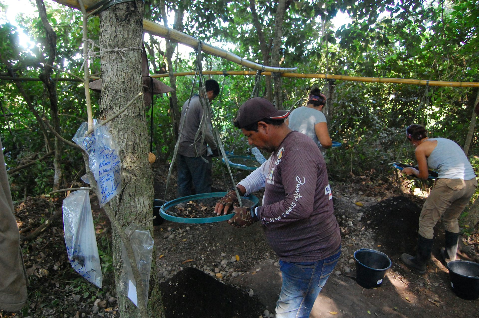 Foto mostra uma pessoa em primeiro plano, trabalhando numa esp&eacute;cie de peneira. Ao fundo, outros homens participam do trabalho de escava&ccedil;&atilde;o