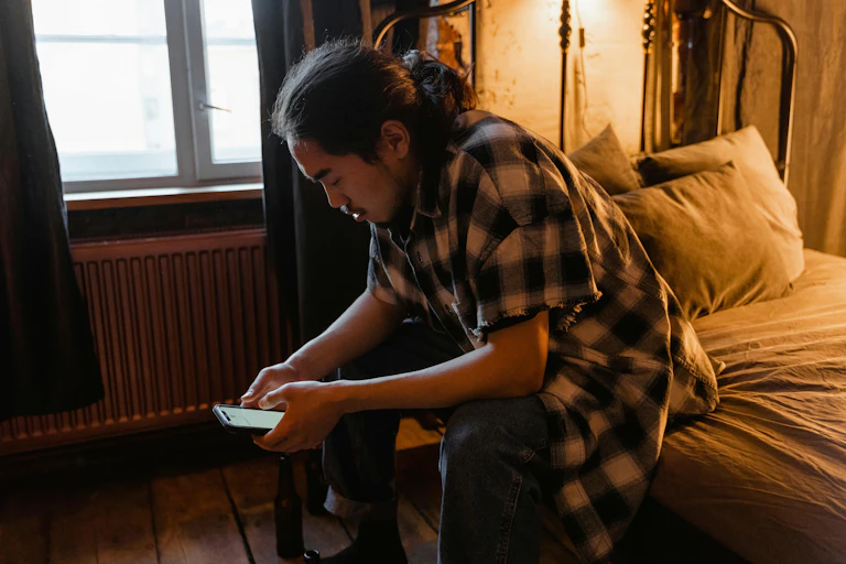 A man sitting on a bed looking at his phone.