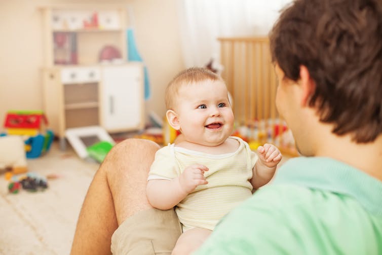 Father holding his baby in his lap, surrounded by toys.