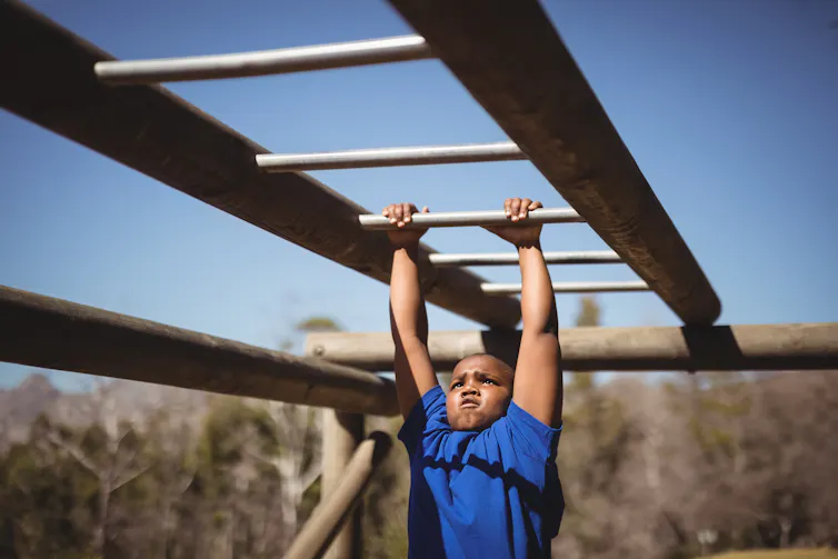 A boy works on the monkey bars at a playground.