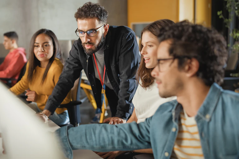 A standing man shows a group of seated people something on a computer screen