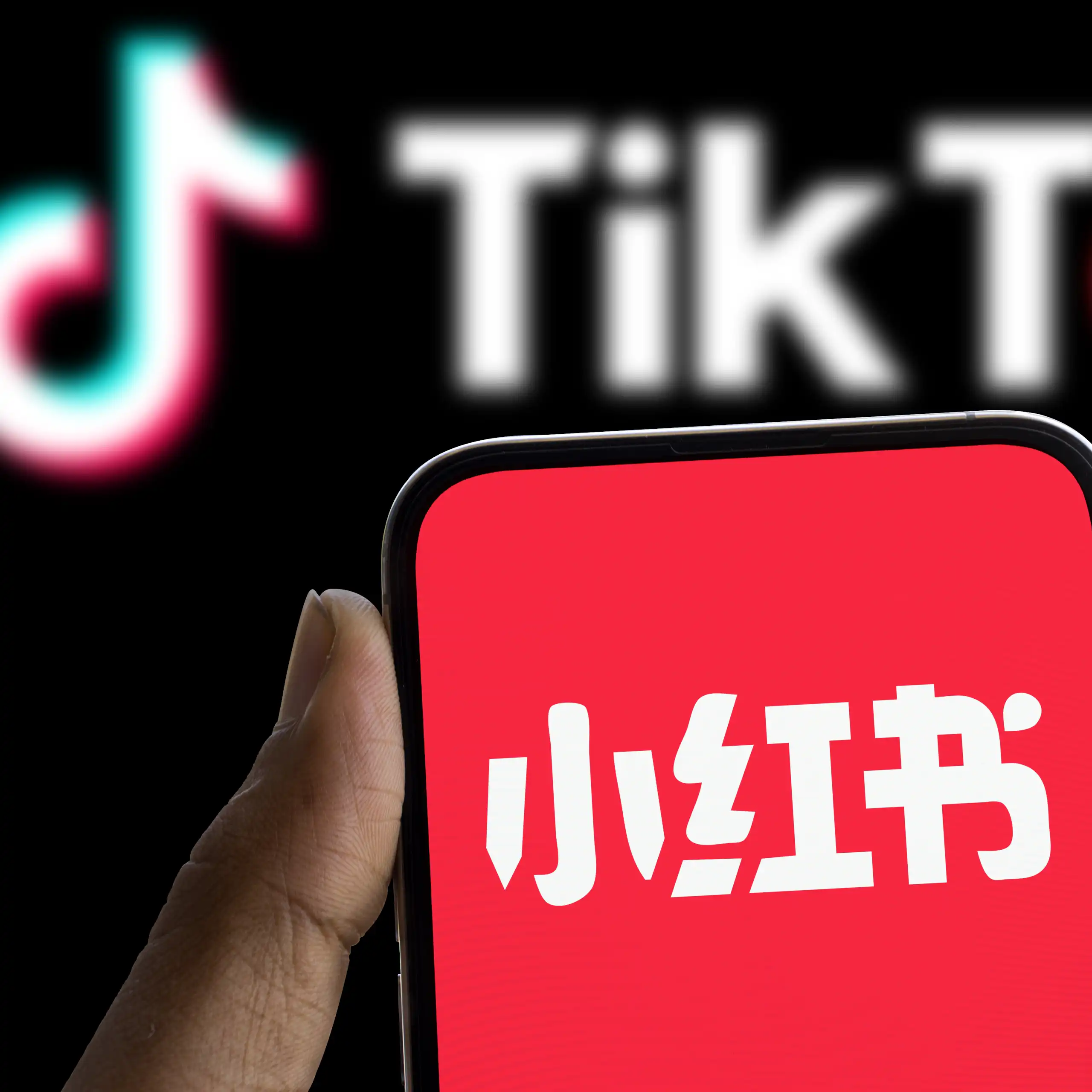 Xiaohongshu logo displayed on smartphone and tiktok logo in the background.