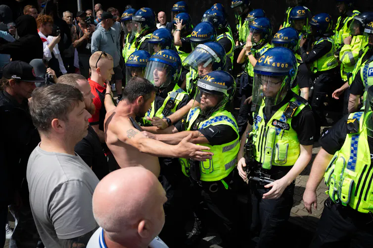 A large group of police scuffling with a shirtless rioter
