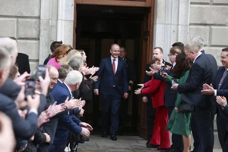 A smiling man is flanked by supporters as he exits a building.