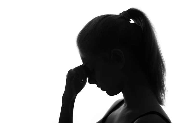 A silhouette of a woman, appearing stressed, holding her head and looking downward.