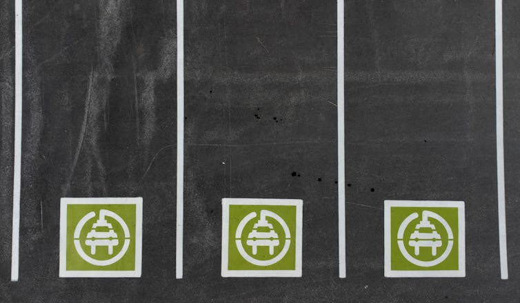Overhead view of three parking spots with green and white symbols painted on them of electric vehicles