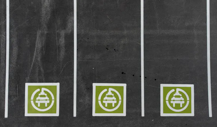 Overhead view of three parking spots with green and white symbols painted on them of electric vehicles